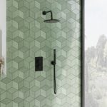a matt black concealed shower including a round shower head and wall arm with a green tiled background