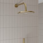 a brushed brass rain fall shower head and wall arm with a white tiled background