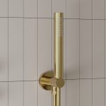 a brushed brass round shower head and outlet elbow with a white tiled background